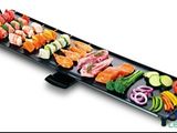 une image représentant un long barbecue noir sur lequel sont disposés divers types d'aliments