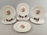six assiettes blanches ornées de chats noirs et de fleurs, posées sur une table
