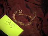 bracelet en chaîne d'or auquel est attaché un petit mot sur un morceau de tissu marron