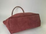 pink sued handbag with brown leather handles on a white surface