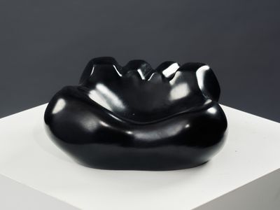 une sculpture noire posée sur un socle blanc, sur un fond gris