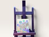 un chevalet violet sur lequel est posé un tableau, devant un mur blanc