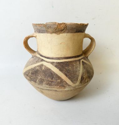 un vase marron muni d'une anse marron, posé sur une table blanche