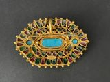 a close up of a gold broochle with a turquoise stone in the center