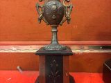 un vase en bronze posé sur un piédestal sur un tapis rouge