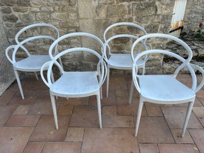 quatre chaises blanches posées sur un sol en briques, près d'un mur en pierre