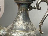 a silver tea pot sitting on a table next to a candle
