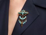 a close up of a woman wearing a blue jacket and a turquoise broochle