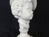white marble bust of a boy wearing a hat on a black background