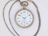 a silver pocket watch with a chain around it on a white surface