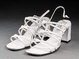une paire de sandales en cuir blanc à lanières, posées sur un fond gris