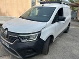 La camionnette blanche est garée devant un immeuble ; elle est équipée d'une galerie de toit.