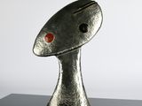 silver sculpture of a fish with a red eye sitting on a black surface