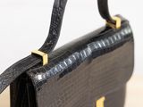 black leather handbag with gold handles on a wooden table