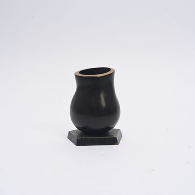 vase noir reposant sur un socle en bois, posé sur une surface blanche