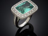 a close up of a ring with a green stone surrounded by diamonds