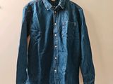 denim shirt hanging on a hanger on a white wall