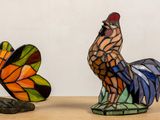 two stained glass sculptures of a rooster and a butterfly on a table
