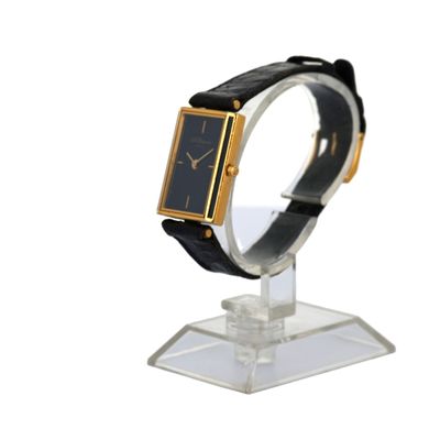 une photo d'une montre noire et dorée posée sur un socle transparent