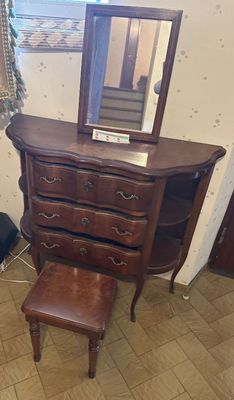 a dresser with a mirror and a stool in a room