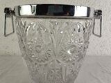 a glass ice bucket with a metal handle on a table