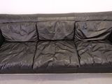 black leather couch with three pillows on top of it in a room