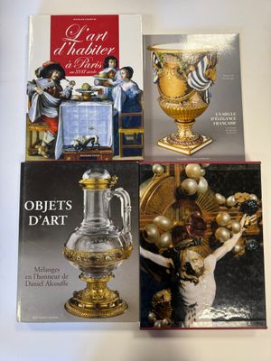 trois livres posés sur une table sur laquelle se trouve un vase doré