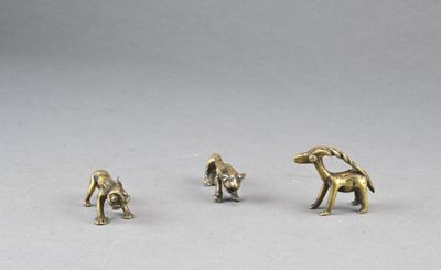 three brass figurines of dogs and a cat on a white surface