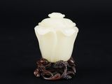 un vase en jade blanc représentant une fleur posée sur un socle, sur fond noir