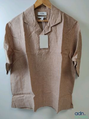 une chemise beige avec une étiquette suspendue à un cintre accroché au mur