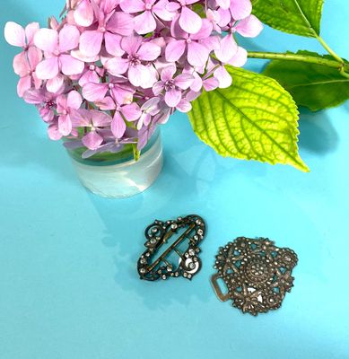 lila flowers in a vase and a brooch on a blue surface