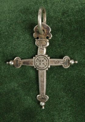 une croix en argent sur du velours vert, surmontée de perles en argent