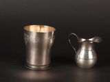 a silver pitcher next to a silver cup on a table