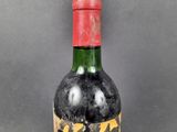 an old bottle of wine with a red cap on a grey background