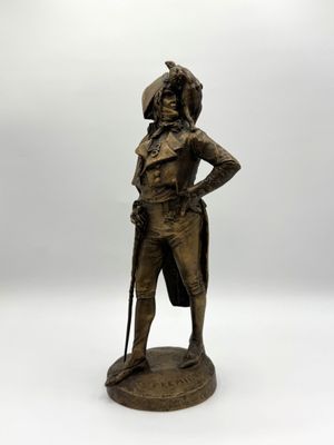 Une statue représentant un homme coiffé d'un chapeau et muni d'une canne se dresse sur une surface blanche