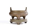un petit pot en bronze posé sur un socle, sur une surface blanche