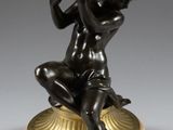 une figurine antique en bronze représentant un garçon assis sur un coquillage