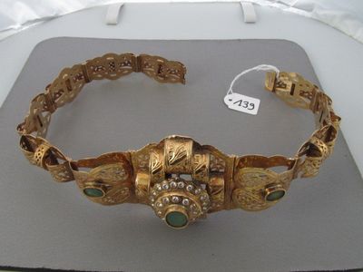 bracelet en or orné de pierres vertes, exposé sur une table