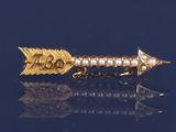 une broche en forme de flèche, en or et perles, sur un fond bleu