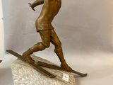 bronze statue of a man on skis on a rock next to a red and white flag