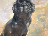 une statue en bronze représentant un garçon assis sur un rocher