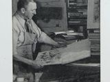 black and white photograph of a man sitting at a desk in front of a map