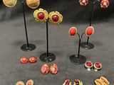 several pairs of gold and red earrings and brooches on stands