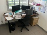 a desk with two computer monitors and a chair in front of a window