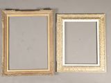 two gold picture frames on a wall next to a mirror