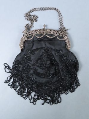 black beaded purse with chain and tassels on a white surface