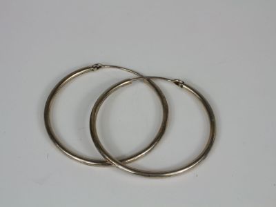 two pairs of silver hoop earrings on a white surface