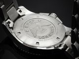 the back of a watch with a metal band on a black surface