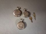 trois montres de poche en argent et une clé posées sur une table