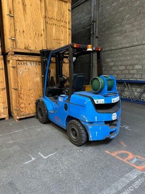un chariot élévateur bleu garé devant une pile de caisses en bois